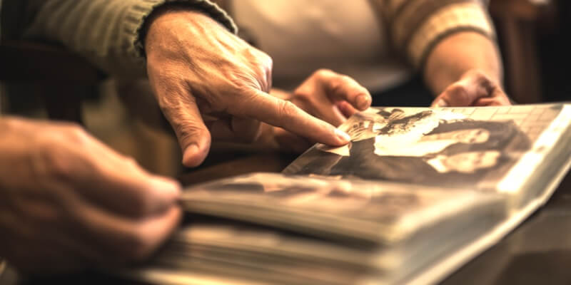 Close-up of elderly hands flipping through a photo album, pointing at old black-and-white photographs, evoking nostalgia and memories.