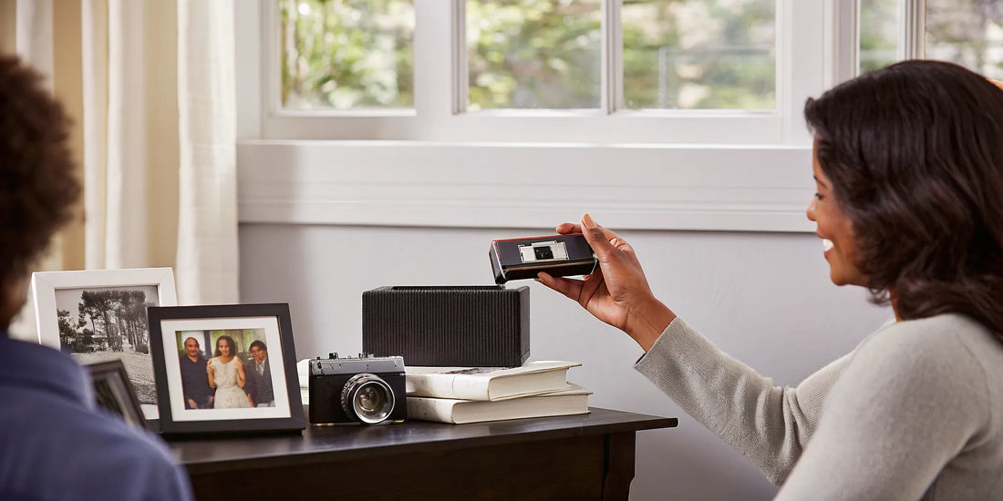 Woman holding a MiniDV tape with a camcorder and family photos in the background.