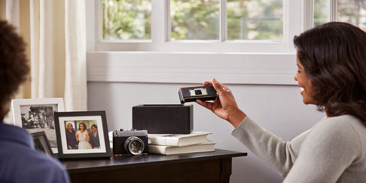 Woman holding a MiniDV tape with a camcorder and family photos in the background.