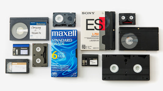 Assorted video cassette formats on a table, including VHS, Betamax, VHS-C, MiniDV, and Hi8/Video8 tapes.